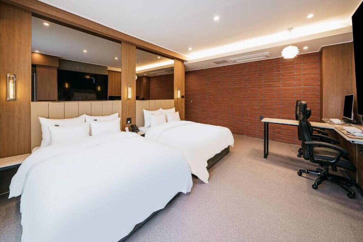 Ein Hotelzimmer mit zwei Betten, einem Schreibtisch, einem Stuhl und einem Fernseher.