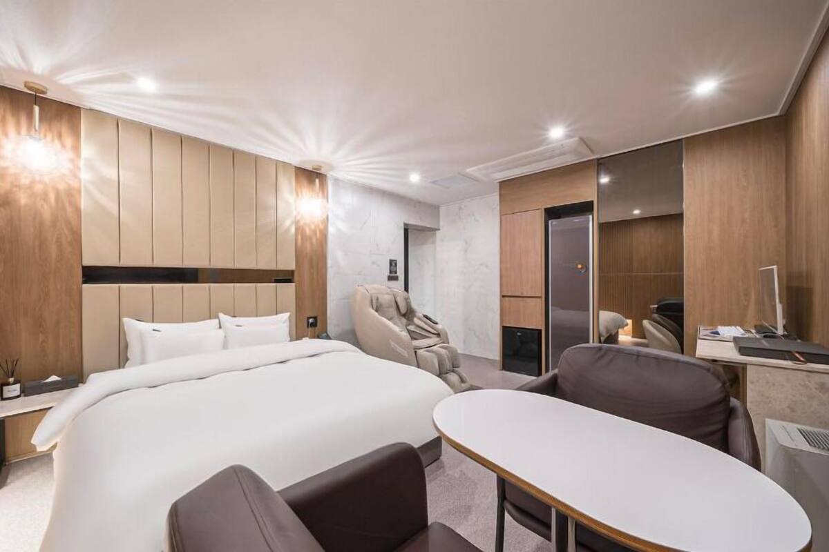 Ein modernes Hotelzimmer mit einem großen Bett, einem Massagesessel, einem Schreibtisch und einem Spiegel.