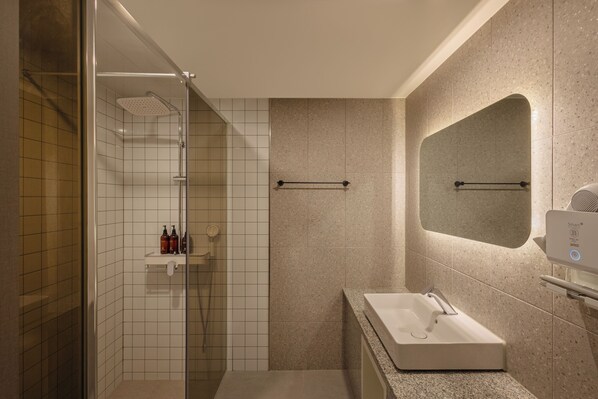 A modern bathroom with a glass-enclosed shower, a vanity with a sink, and a mirror.