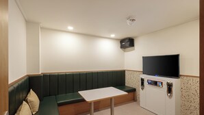 Et lille, privat rum med en grøn polstret bænk, et hvidt bord, et fladskærms-tv og et minibar.