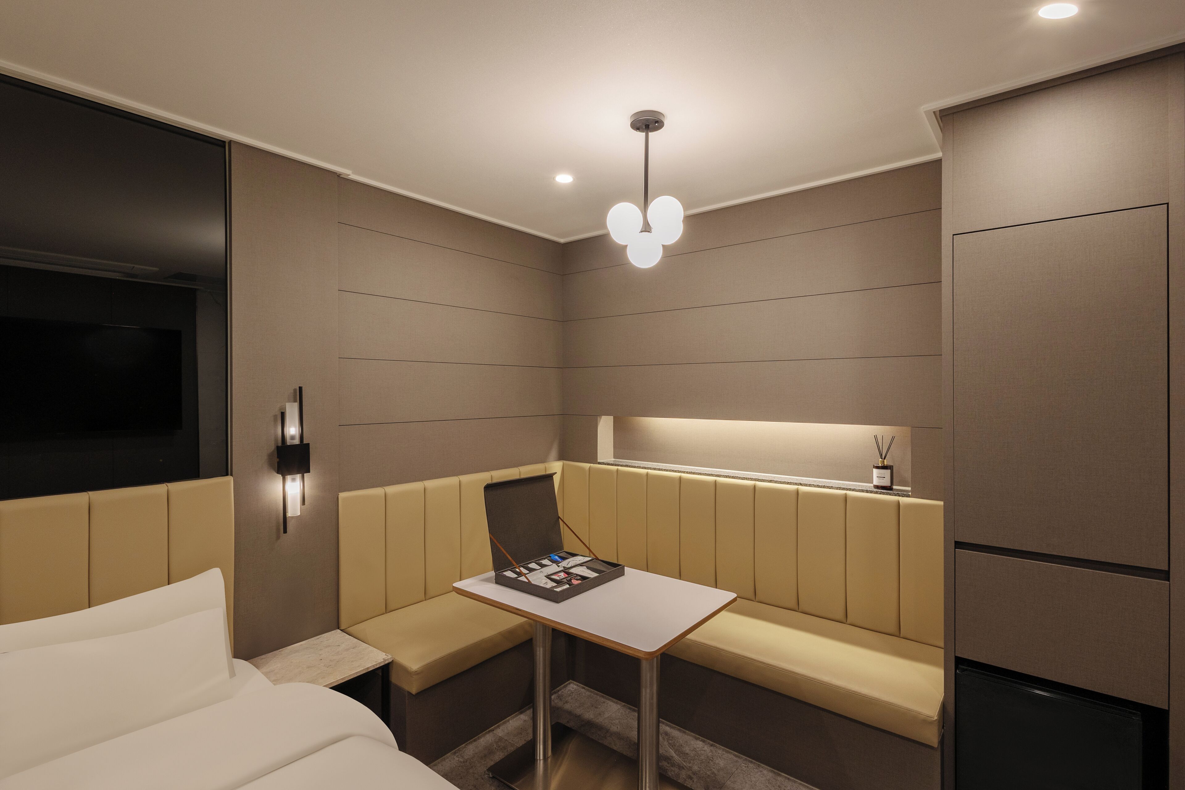A hotel room with a bed, a small table, a bench, a TV, and a refrigerator.