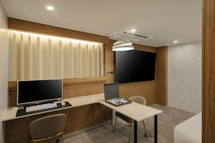A modern office space with a desk, computer, and chair, a large window with blinds, a mounted TV, and a pendant light.