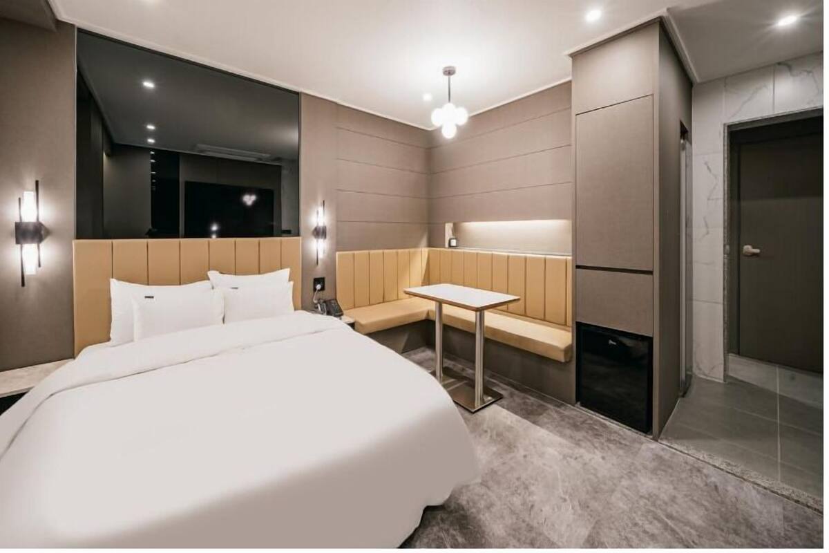Ein modernes Hotelzimmer mit einem großen Bett, einem kleinen Tisch, einer Bank und einem begehbaren Kleiderschrank.