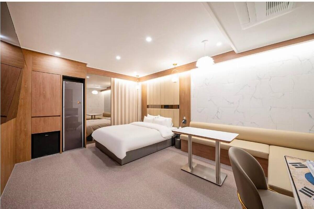 Ein modernes Hotelzimmer mit Bett, Nachttisch, Sessel und Schreibtisch mit Stuhl.