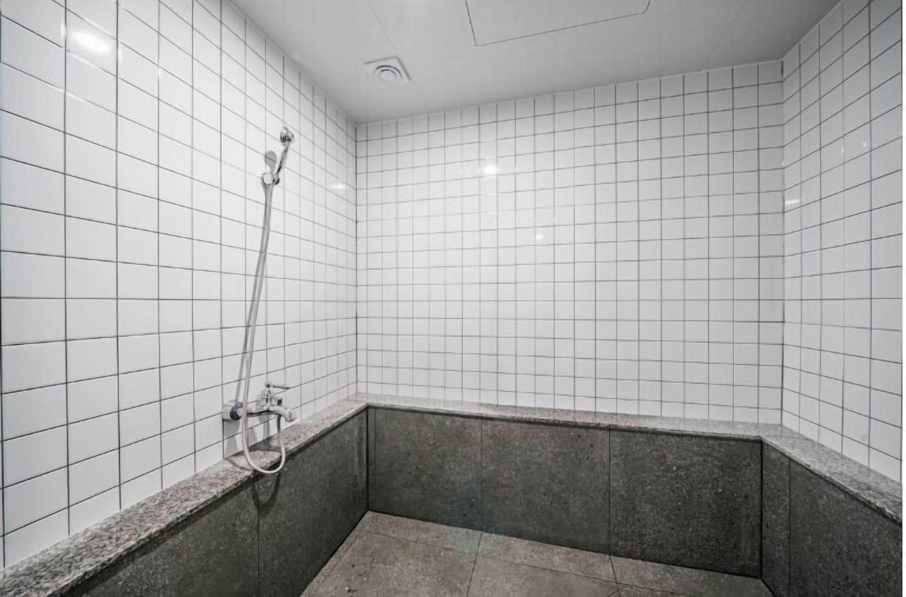 Une petite salle de douche carrelée, équipée d’une seule pomme de douche et d’un lavabo d’angle.