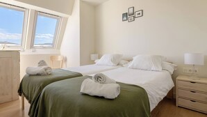 A hotel room with two beds, a wooden wardrobe, a chair, and a window with a view. - Loft Penthouse on the Beach With 2 Terraces (Zarautz)