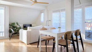 A modern living room with a white sofa, a dining table with chairs, a ceiling fan, and large windows. - Loft Penthouse on the Beach With 2 Terraces (Zarautz)