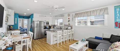 A modern kitchen with white cabinets, a central island, and a dining area with white chairs.