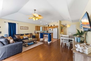 A modern living room with a sofa, coffee table, and a kitchen area with a bar. - Spacious 3BR Beach Condo with Private Deck & Garage Parking (Wildwood)