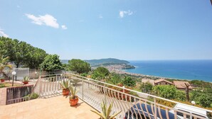 A balcony with potted plants, a railing, and a view of the sea and distant town. - Beautiful home in Agropoli (Agropoli)