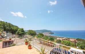 Ein Balkon mit Blumentöpfen, einem Geländer und Blick auf das Meer und eine ferne Stadt.