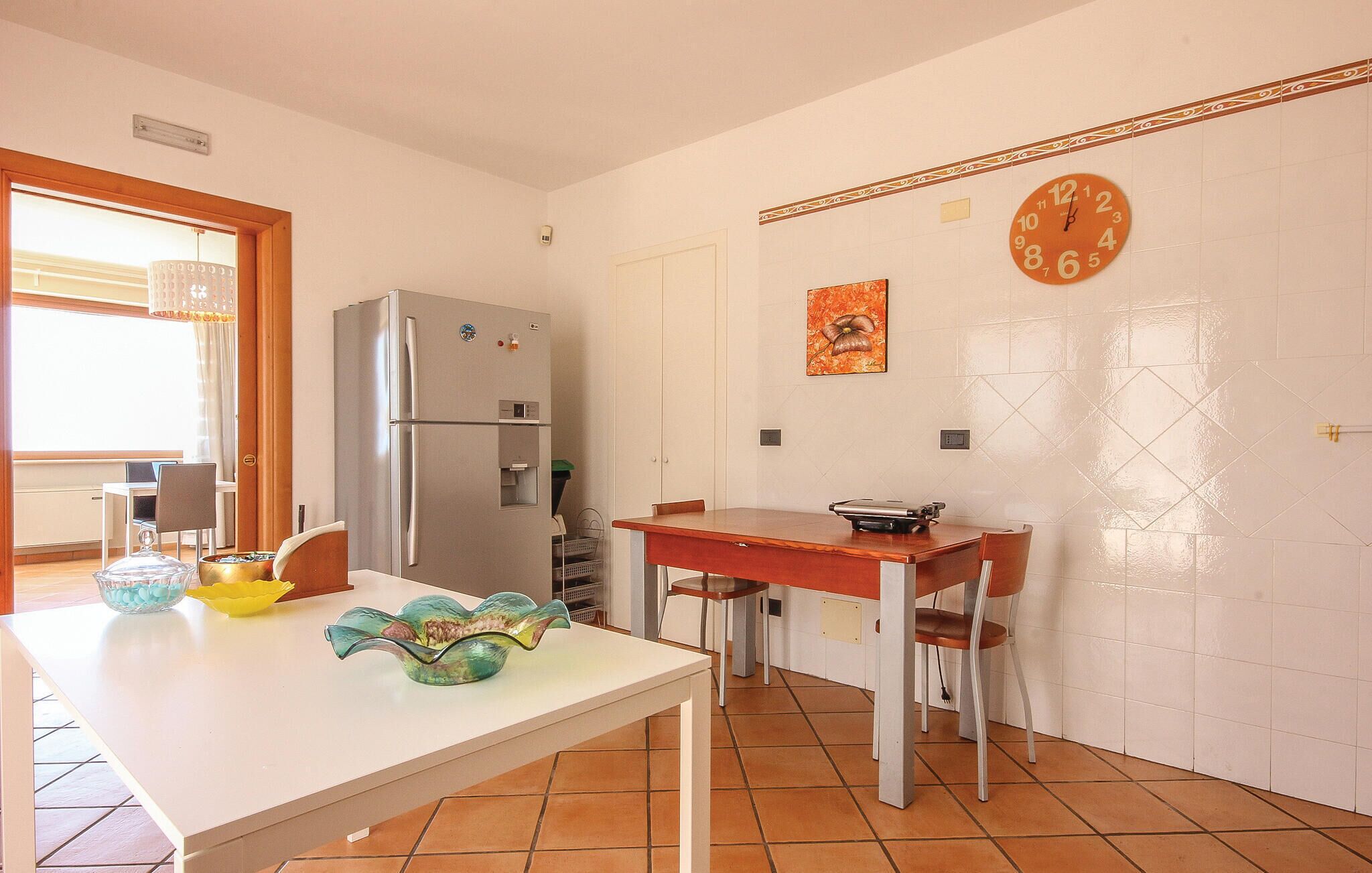 A compact kitchen with a refrigerator, a dining table, chairs, and a wall clock.