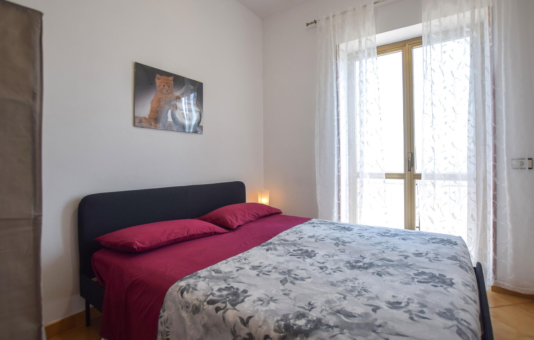 Une chambre à coucher avec un lit, une table de chevet, un tableau et une fenêtre avec des rideaux.
