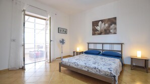 Ein Schlafzimmer mit Bett, Ventilator, einem Bild an der Wand und einer Tür zu einem Außenbereich.