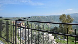 Ein Balkon mit Blick auf eine hügelige Landschaft, ein Gebäude mit Solaranlage und ein Baum.