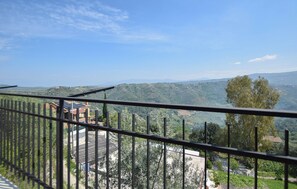 A balcony with a view of a hilly landscape, a building with solar panels, and a tree.