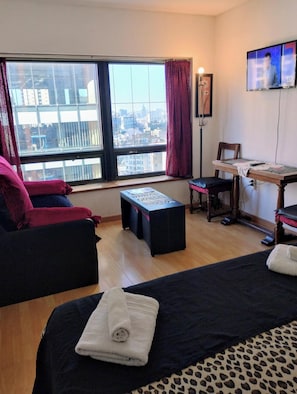 Ein Hotelzimmer mit großem Fenster, einem Bett, einem Schreibtisch und einem Stuhl.