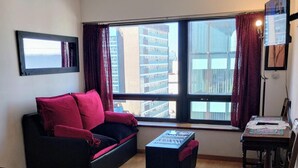 A hotel room with a bed, a sofa, a small table, and a chair. There is a window with curtains and a view of buildings. - Studio in the sky: Obelisco - Av Corrientes. Microcentro CABA. Argentina. (Buenos Aires)