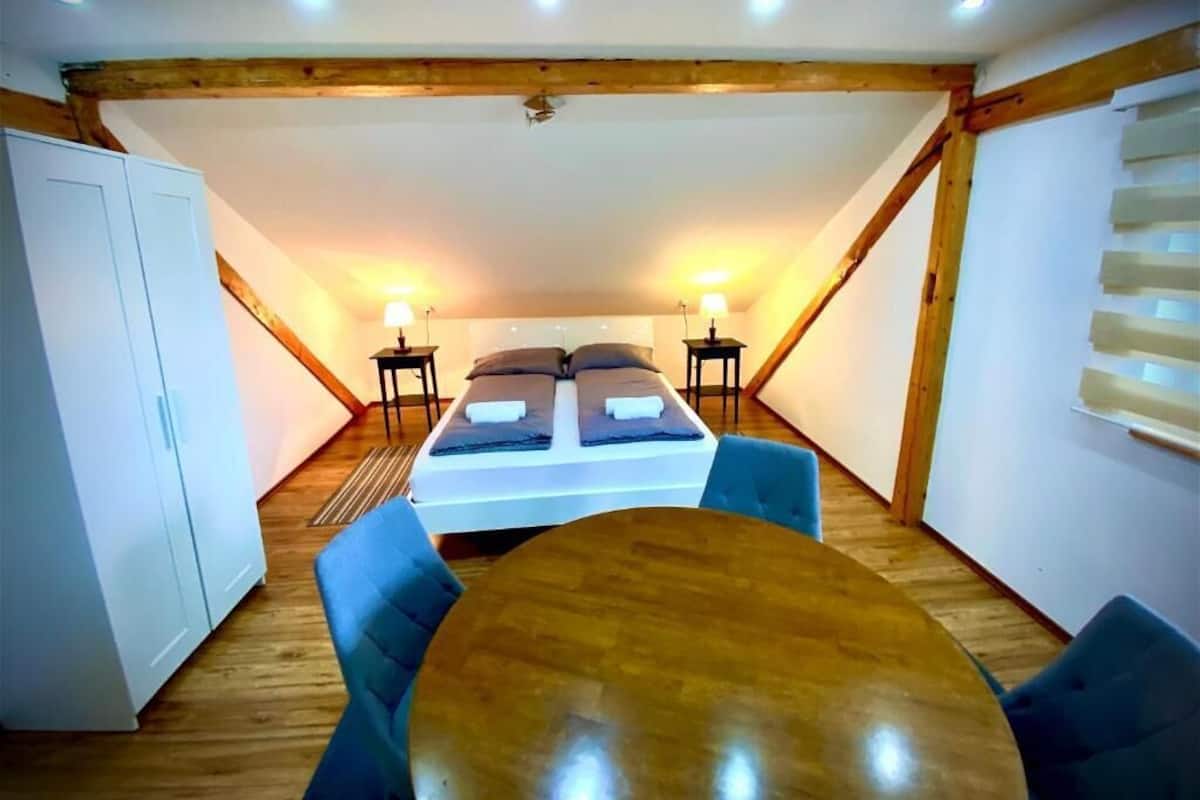 Ein Zimmer mit Holzboden, einem Bett mit Kissen, einem Tisch und zwei Stühlen.