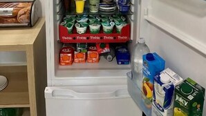 Avoinna oleva jääkaappi, jonka hyllyillä on erilaisia elintarvikkeita ja juomia.