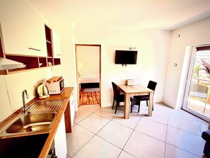 A compact kitchen with a sink, microwave, and toaster, a dining area with a table and chairs, and a TV mounted on the wall. - House by the river  (Plitvica Selo)