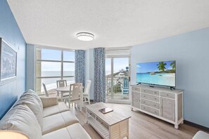 Ein Zimmer mit Balkon, Fernseher, einer Couch und einem Esstisch.