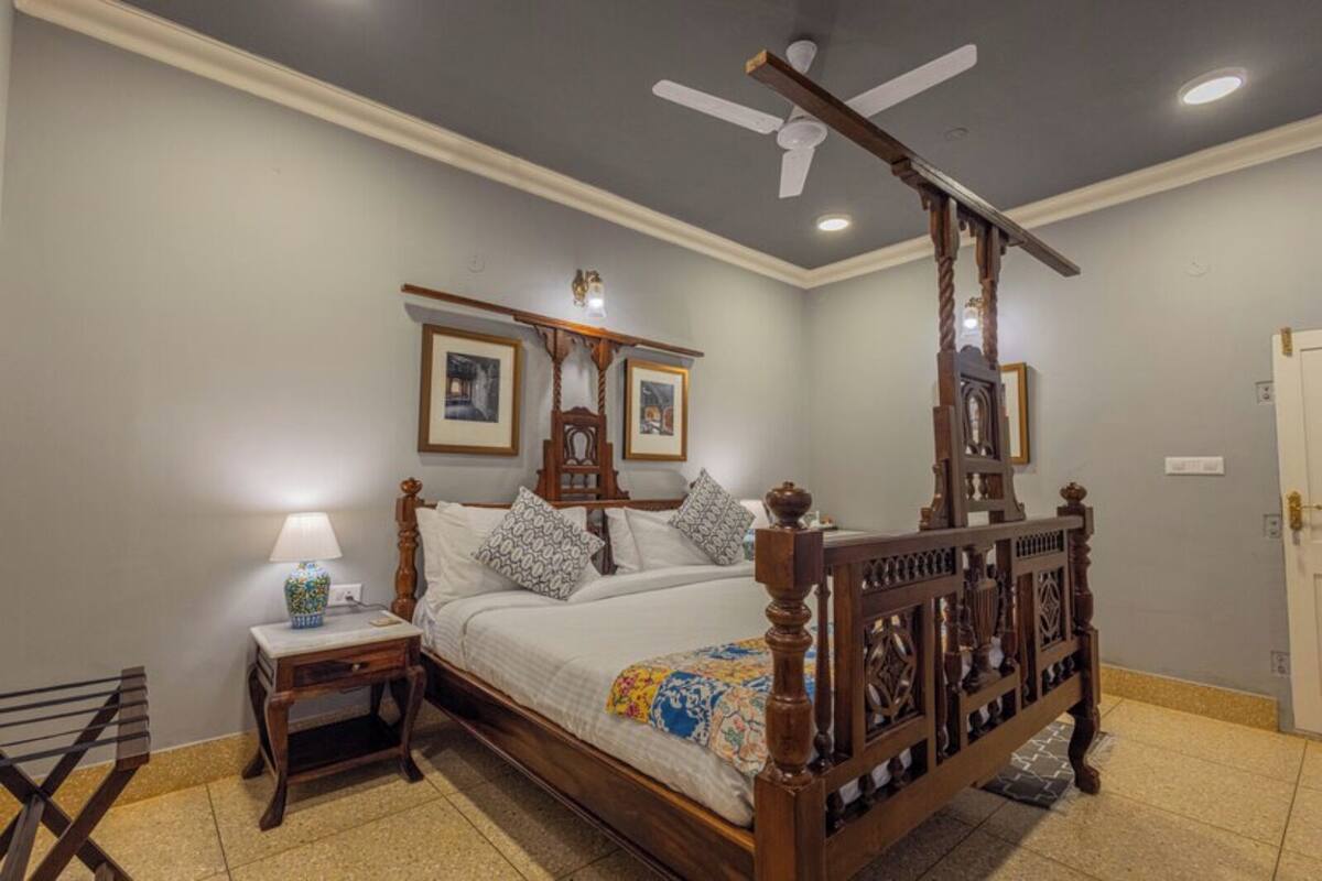 Ein Bett mit Baldachin, ein Holzkopfstück, ein Nachttisch mit Lampe und ein Deckenventilator.