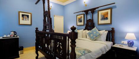 A bedroom with a four-poster bed, a nightstand with a lamp, a dresser, and framed pictures on the walls.
