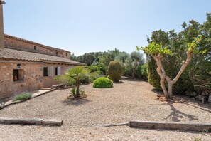 A courtyard with a stone building, gravel ground, and various trees and shrubs. - CAN PUIG - Lovely house with private pool and free Wi-Fi (Santanyí)