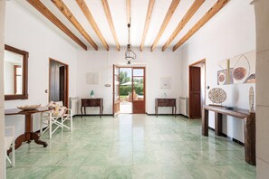 A spacious room with a high ceiling, wooden beams, a green-tiled floor, and a view through a doorway to an outdoor area. - CAN PUIG - Lovely house with private pool and free Wi-Fi (Santanyí)