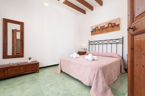 Een slaapkamer met een bed, een houten dressoir, een spiegel, een schilderij en een houten deur.