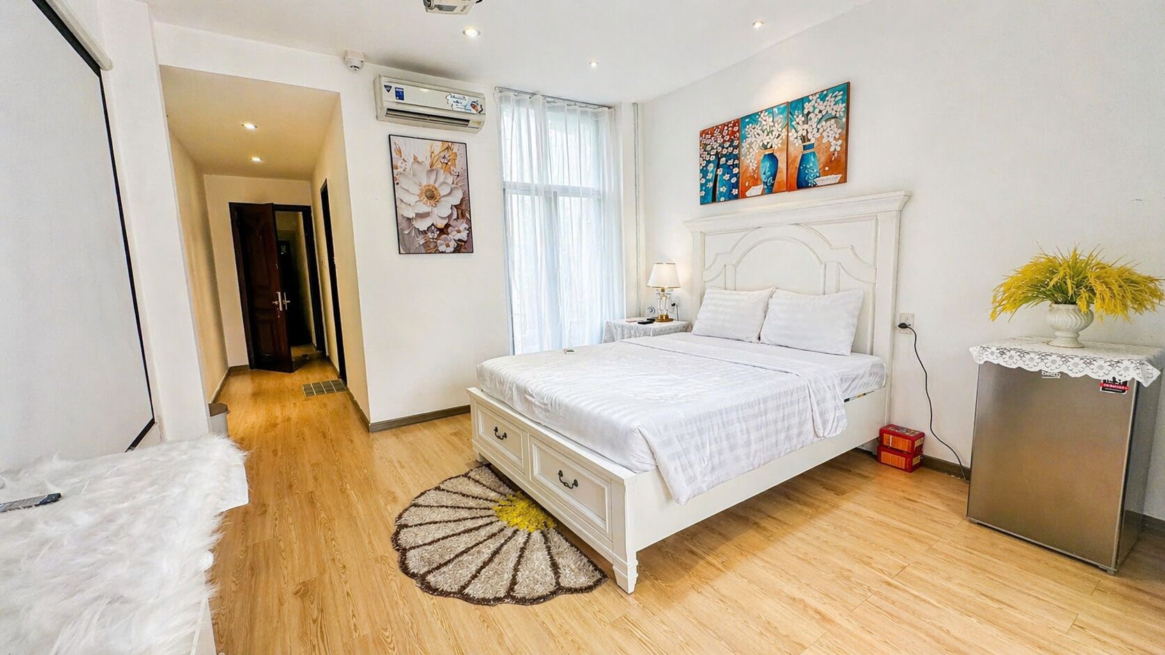 Ein Schlafzimmer mit Bett, Nachttisch, Kommode, Heizkörper, einem Fenster mit Vorhängen und einem Bild an der Wand.