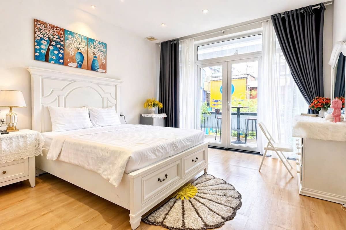 A bedroom with a bed, bedside tables, a lamp, a painting, a window with curtains, and a view of the outside.