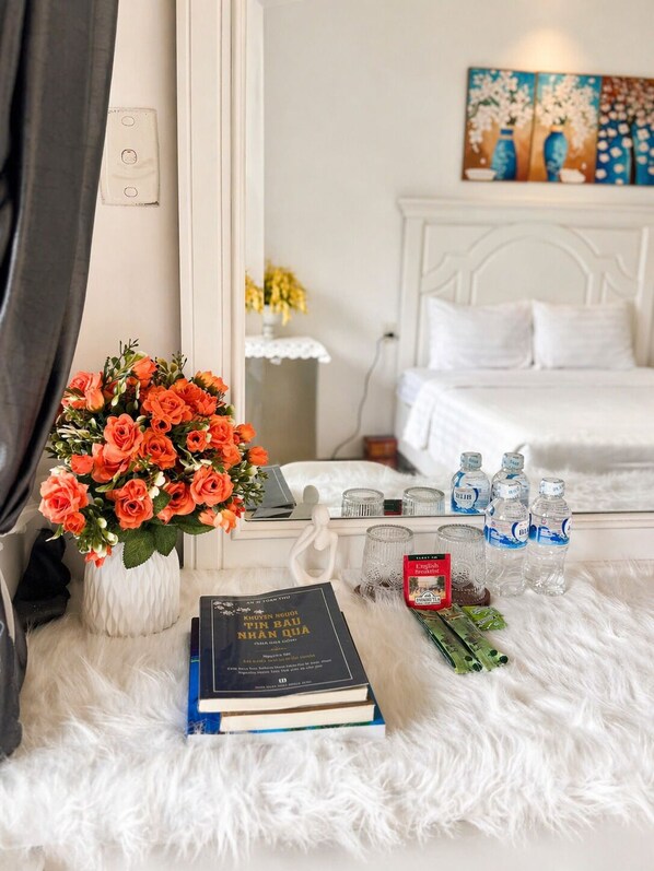A hotel room with a bed, a bedside table with a vase of flowers, a book, a glass of water, and a painting on the wall. - Movida Stay - Bui Vien Walking Street, District 1 (Thanh Pho Ho Chi Minh)