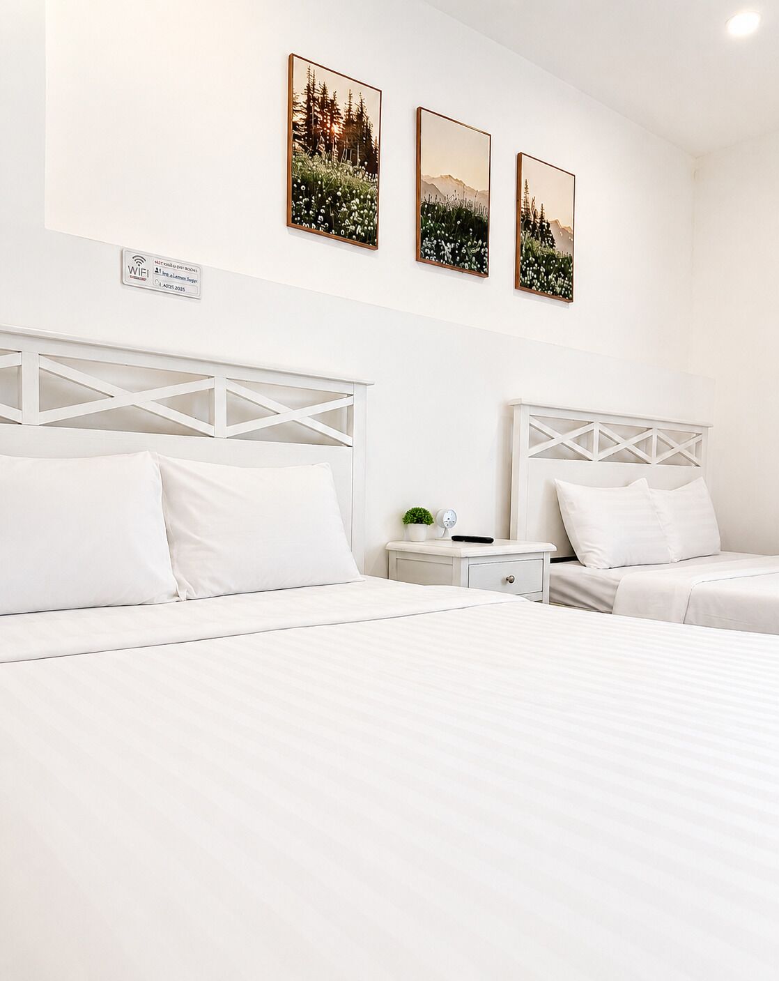 A hotel room with two beds, a nightstand, a small table, and three framed pictures on the wall.
