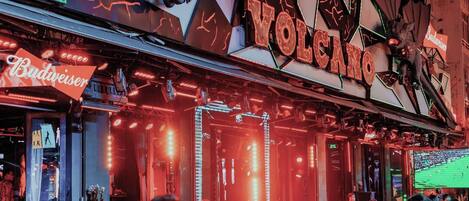 A venue with a neon sign reading 'VOLCANO' and a Budweiser sign.