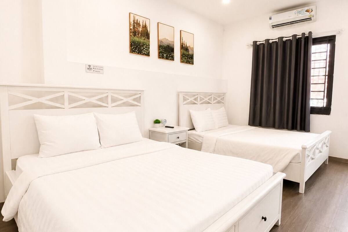 A hotel room with two beds, a nightstand, a small table, and a window with curtains.