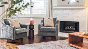 A living room with two armchairs, a small table, a fireplace, and a ceiling fan.