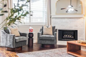 A living room with two armchairs, a small table, a fireplace, and a ceiling fan. - Luxury Family Retreat • Saltwater Pool Oasis • BBQ (Frisco)