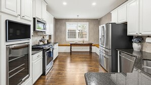 A modern kitchen with white cabinets, stainless steel appliances, and a wooden floor.