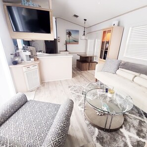 Una sala moderna con sofá, sillones estampados, una mesa de centro, televisor, área de cocina y mesa de comedor.