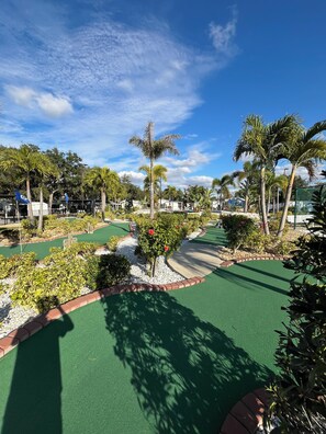 Ein Minigolfplatz mit grünem Kunstrasen, Palmen und blauem Himmel.