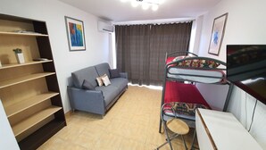 Un espacio habitable pequeño con sofá, literas, escritorio y estantería.