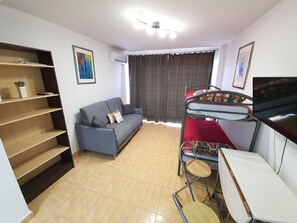 Een kleine woonruimte met een bank, een stapelbed, een bureau en een rek.