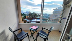 A balcony with two chairs, a small table, and a view of buildings and palm trees. - TRAMUNTANA 325 STUDIO (Roses)