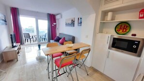 A compact living space with a dining area, a sofa, a TV, and a microwave. - TRAMUNTANA 325 STUDIO (Roses)