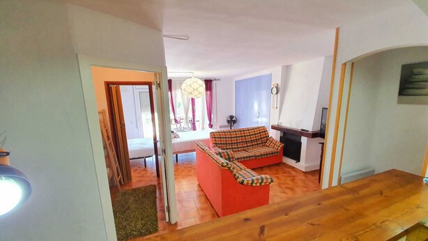Un salon comprenant un canapé, une cheminée et un coin repas visible à travers une porte ouverte.