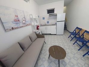 Ein kleiner Wohnraum mit einer Couch, einem runden Tisch, einer Küchenzeile und einem Bild an der Wand.