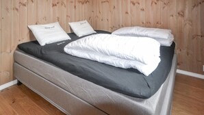 A bed with a black mattress and white pillows, set against a wooden wall.