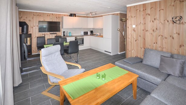 A modern living room with a sofa, a wooden coffee table, and a dining area with chairs and a table.